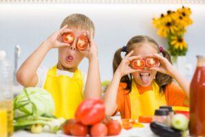 Happy kids having fun with food vegetables at kitchen holds tomatoes before his eyes like in glasses
