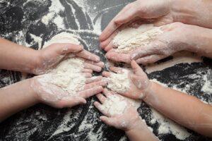 Many hands with handfuls of flour, family cooking dough, bread and festive cookies.